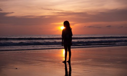 A woman standing on a beach at sunset.