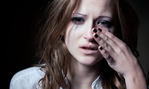 Photo of a young woman wiping tears of her eyes.