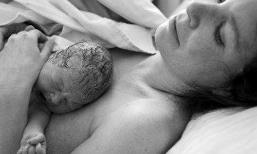 Greyscale photo of a woman lying down with her newborn baby.