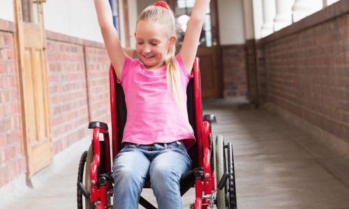 Photo of a girl in a wheelchair with her arms in the air looking happy.