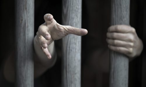 Photo of a persons hands reaching through prisons bars.