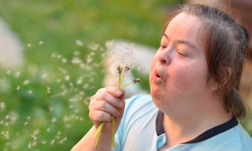 Woman with intellectual disability blowing on a dandelion.