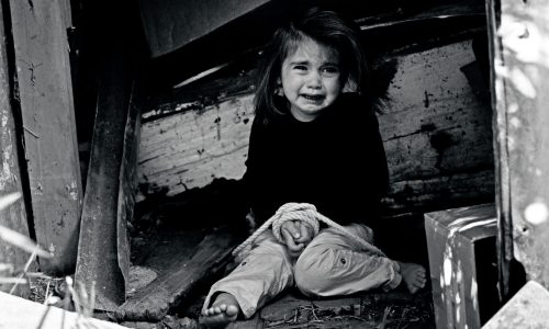Greyscale photo of a young girl tied up. She is crying and looking scared.