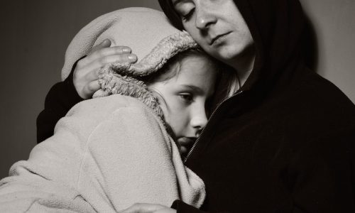 Photo of a woman in a hooded jumper holding her daughter on her lap.