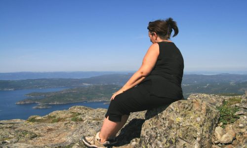 Woman sitting on a rock mountain looking out into the distance.