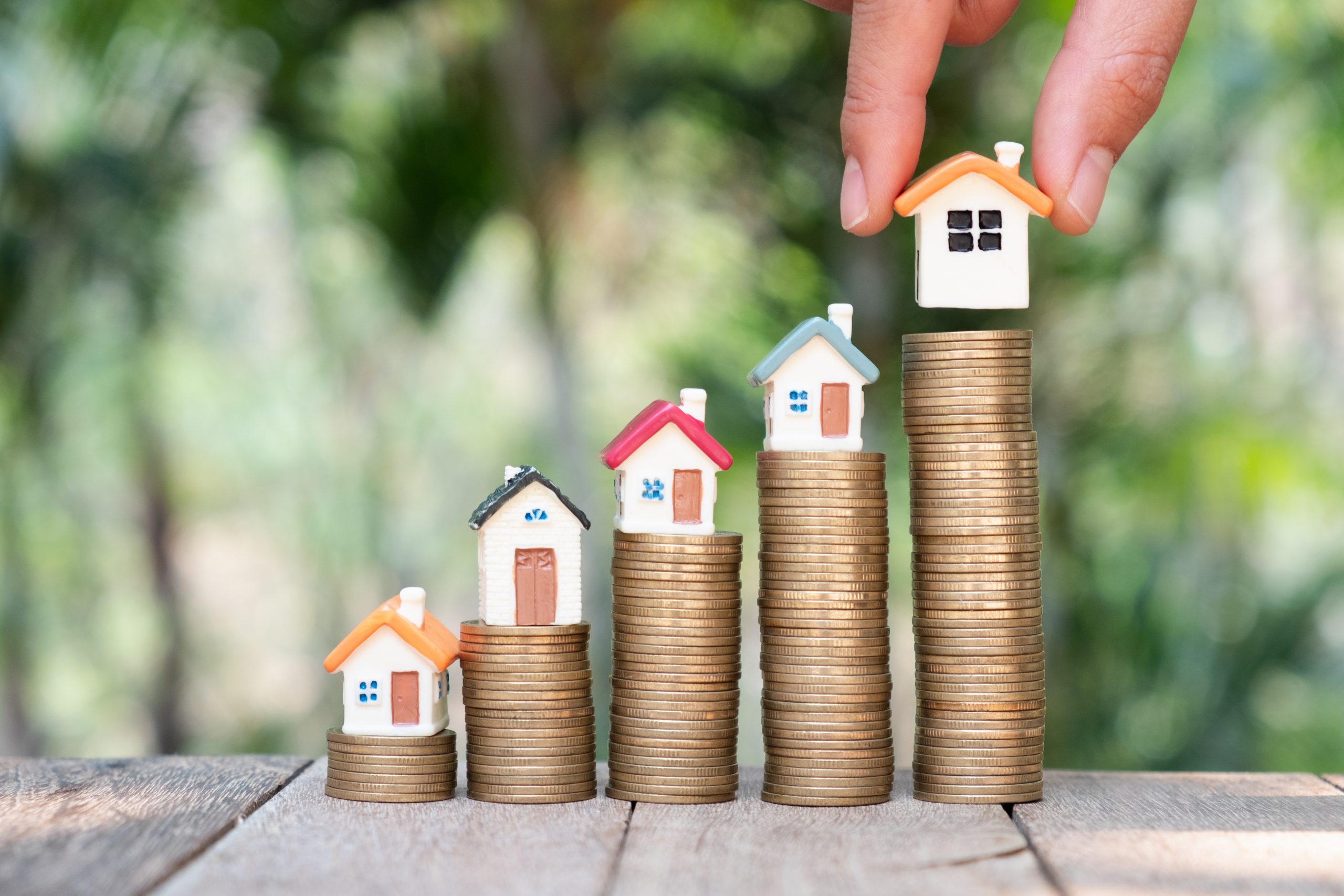 Photo of 5 piles of coins with small statues of houses on top of them.