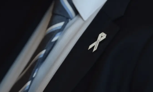 Photo of a white ribbon pinned to a mans suit jacket.