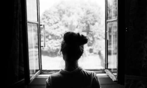 Greyscale photo of a woman looking out of an open window.