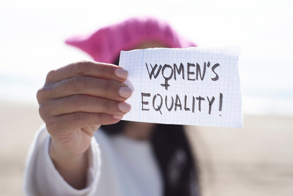 Close up of a woman holding a peice of paper with the words 'Women's Equality' on it.