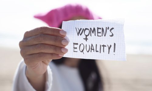 Close up of a woman holding a peice of paper with the words 'Women's Equality' on it.