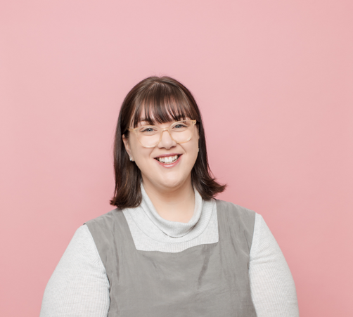 Portrait style photo of WWDA staff member, Mali Hermans. A young woman with shoulder length brown hair wearing a white top, with a grey tunic and glasses.