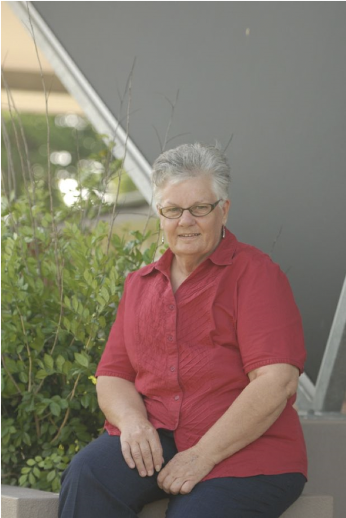 Photo of Jude Marshall, wearing a red shirt and glasses with short grey light hair.