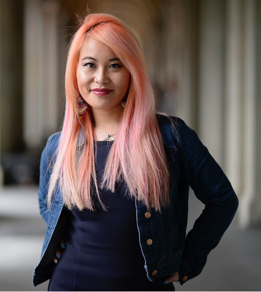 Akii Ngo (Image description a woman with long pink straight hair who is smiling. Akii is wearing a blue demin jacket and a blue top and earrings and a necklace)