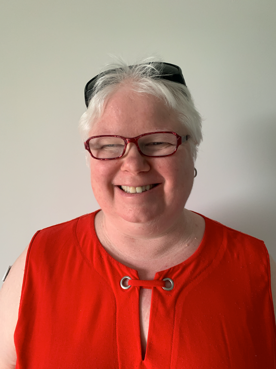 Raelene Brock (image description. An image of a woman with light coloured hair who is smiling. Raelene is wearing glasses and is wearing a red top and is standing in front of a white wall