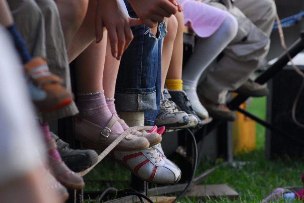 A photo of children sitting on a bench. The shot has been taken from their knees down so you can only see their legs and feet. 