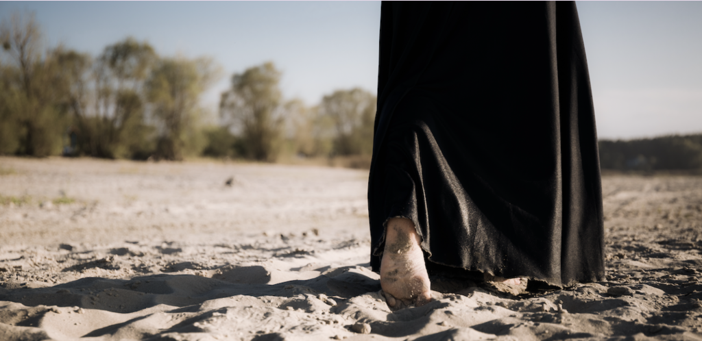 A woman with a long black dress walking on the beach