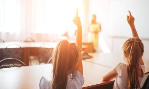 A photo of two young girls with their hands raised in a classroom