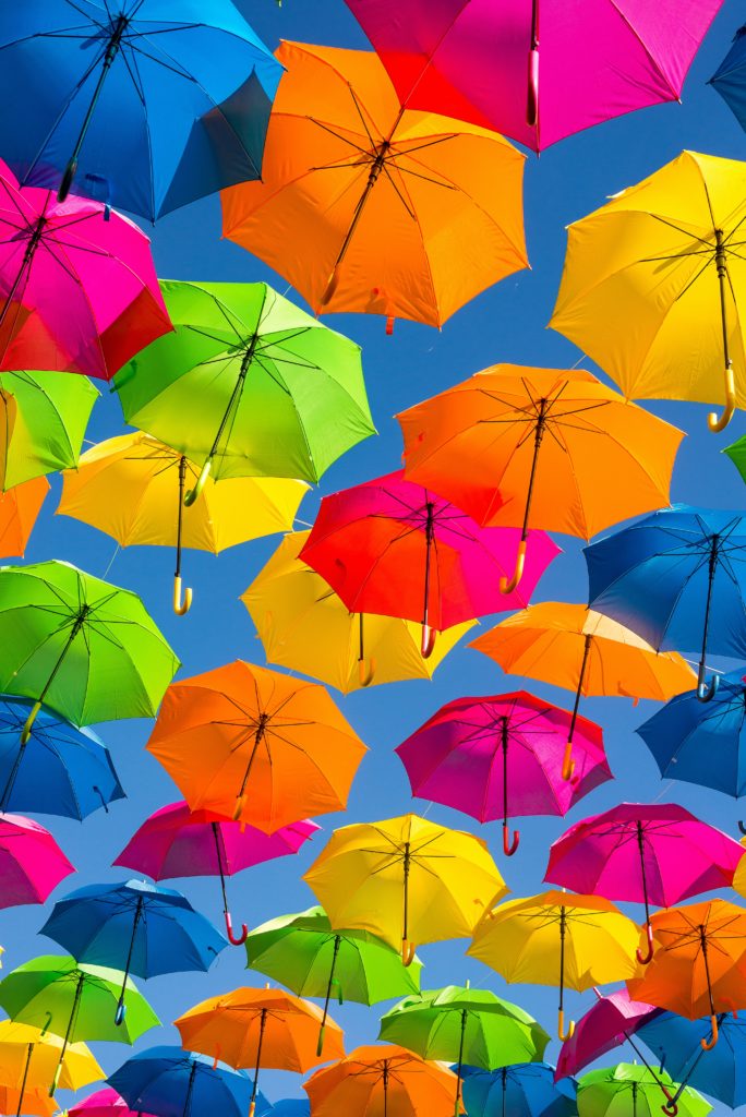 Photo source: Guy Stevens. A photo of lots of colourful umbrellas up in a blue sky. 