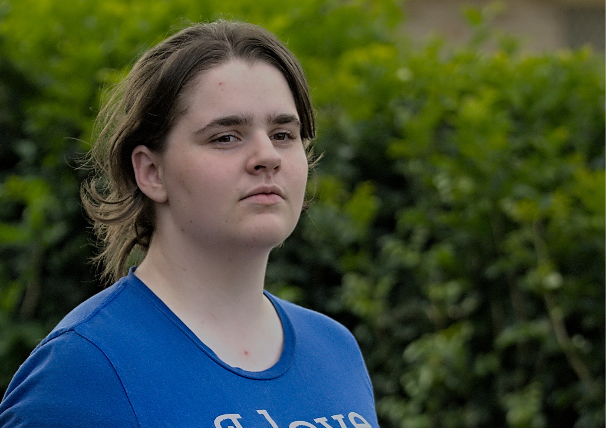 Photo of Maria who has dark brown hair tied back in a ponytail and is wearing a blue shirt that reads I love someone who is autistic (it's me).