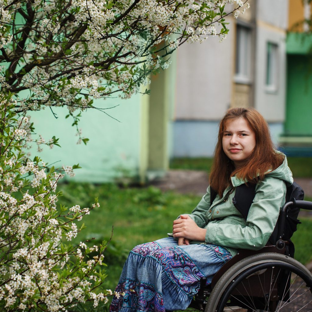 Photo of a young girlw ith brown hair sitting in a wheelchair in the garden under a blossoming tree