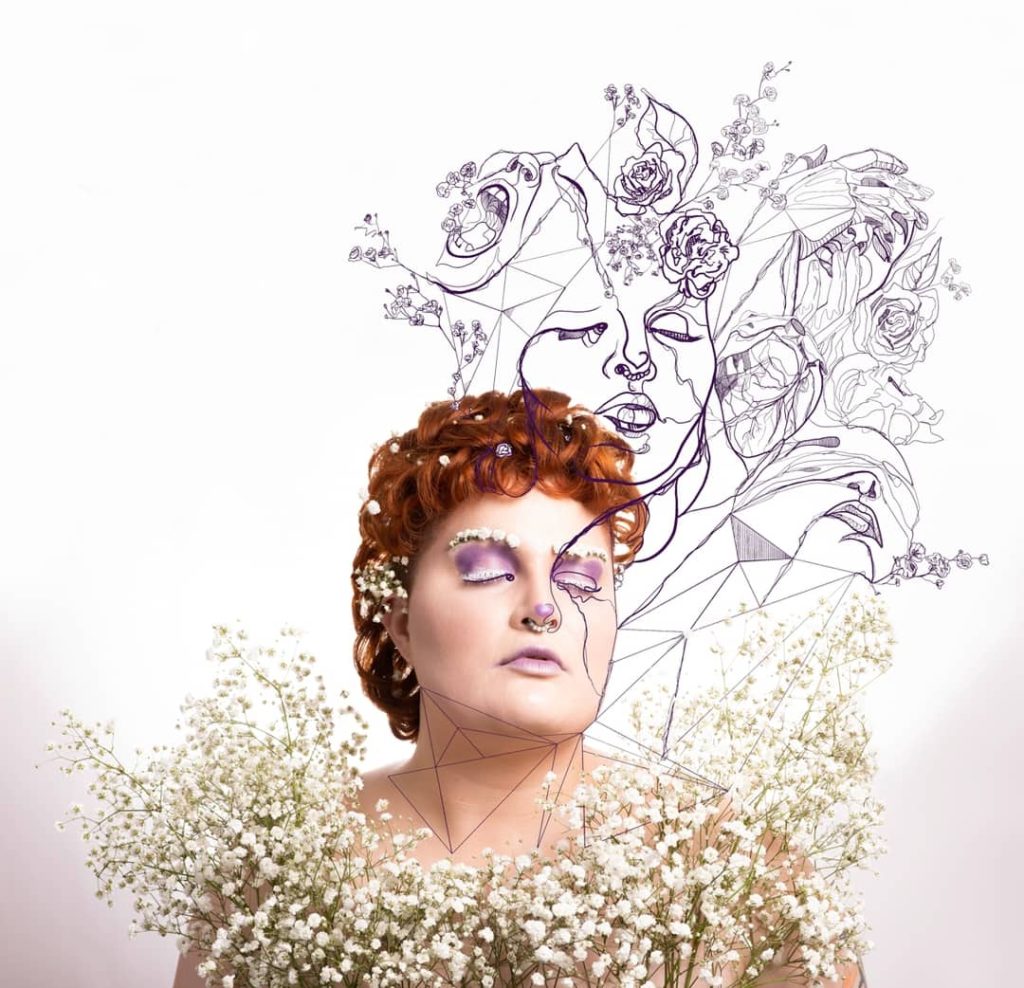 The image shows Marla, with fair skin and a curly copper mullet, with white flowers across their chest, in their hair and sitting across their brows. They are wearing purple eyeshadow and lipstick. They have their eyes closed, and on top of the photo is fine line illustrative work depicting different emotions and struggle, validating those who live with invisible illnesses.