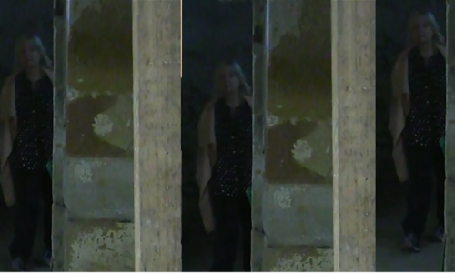 Beyond a blurred wall – which could be interpreted as bars or mirrors – is the figure of Sandie. She is obscured, but you can make out her shoulder-length grey hair.