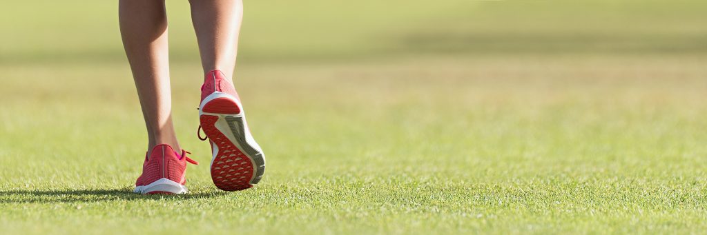 A person wearing red running shoes is jogging on grass during a workout. Only their legs and shoes are visible.