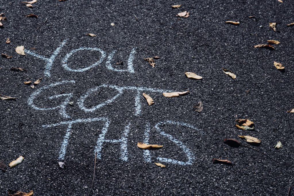 On black bitumen, 'You got this' is written in white chalk. Leave are scattered across the road.