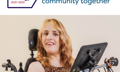 Photo of a woman using an electric wheelchair with a communication device in front of her. She has blonde wavey hair and is wearing a brown and cream top. Above the photo is text: 'Australia's Disability Strategy 2021-2023: Creating an Inclusive Community Together'