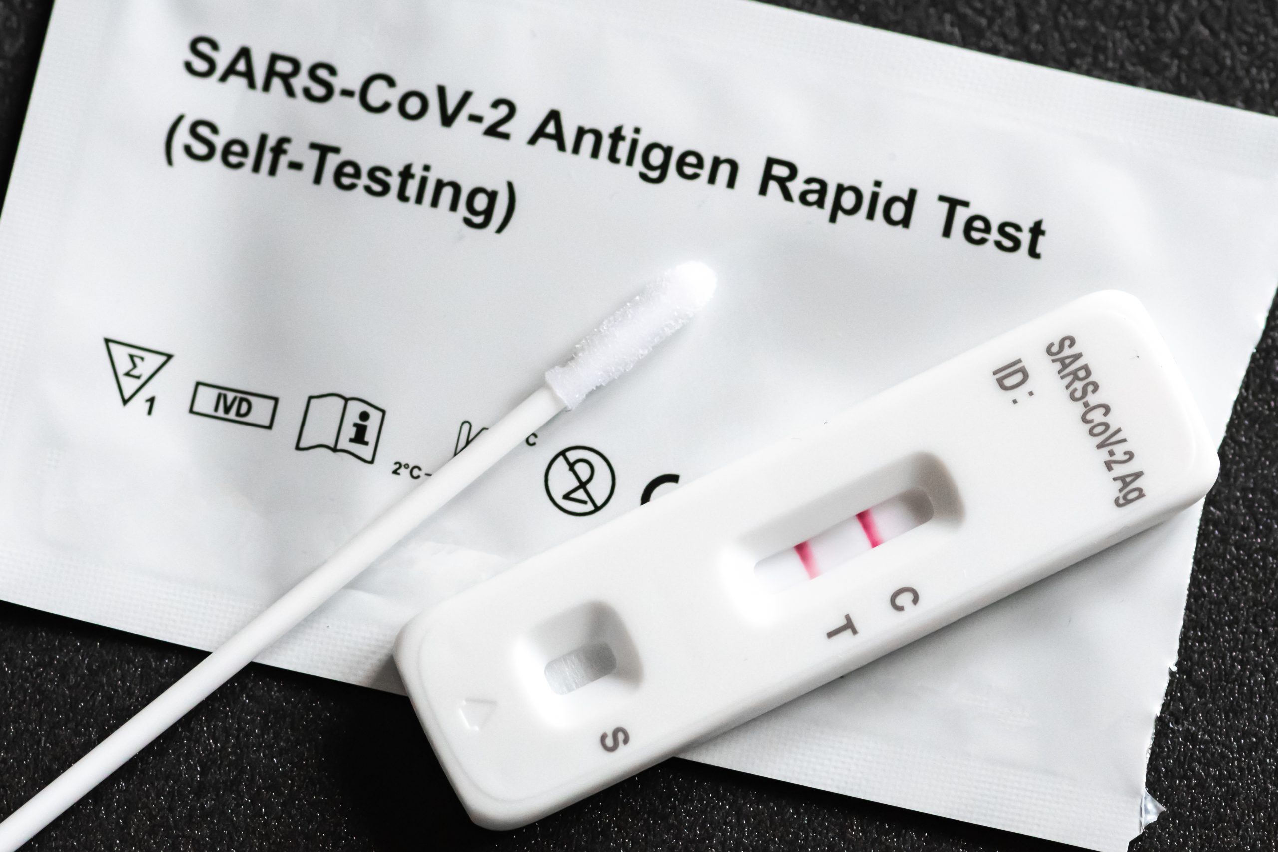 A COVID-19 rapid antigen test kit. A nasal swab and positive test cassette sit on top of the packet that has been torn open.