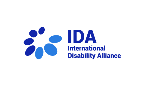 An image of the International Disability Alliance logo. On a white background, blue text reads "IDA International Disability Alliance." An illustration of multiple blue ovals in different shades is next to the text.