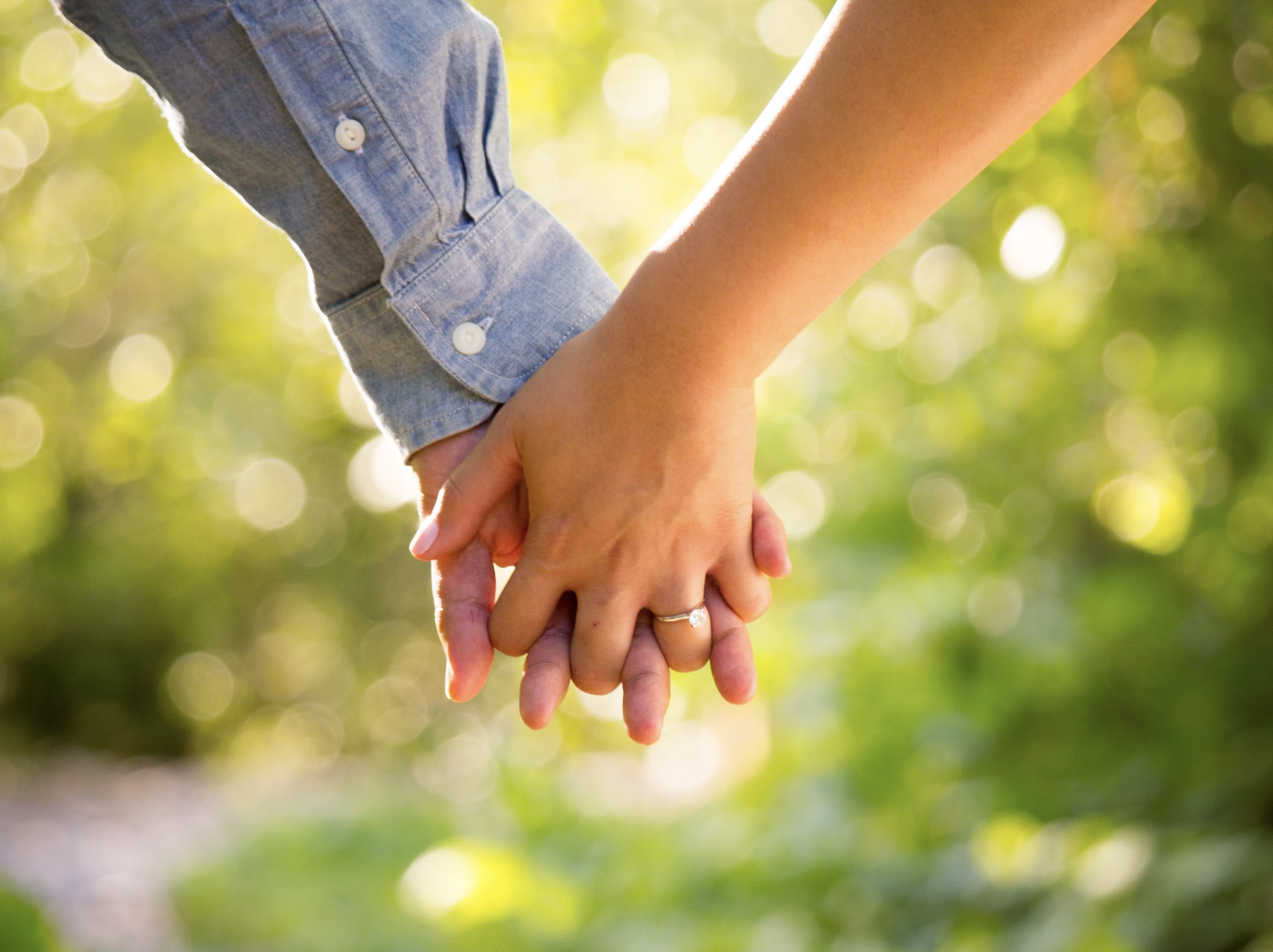 A photo of two hands interlocked. Two white people are holding hands.