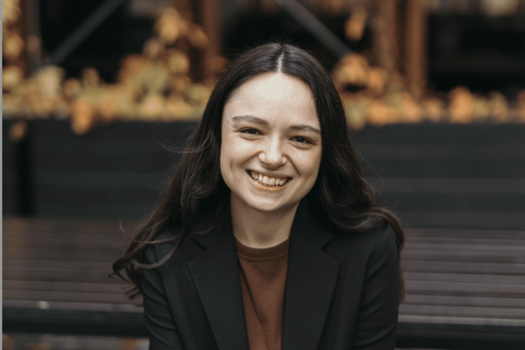 Sophie Cusworth smiling, wearing brown shirt and black blazer. She has light skin and long dark brown hair